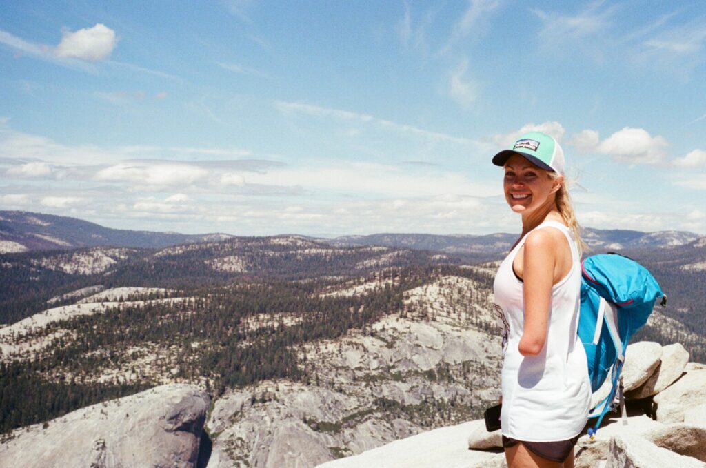 A woman stands on top of Yosemite's Half Dome smiling