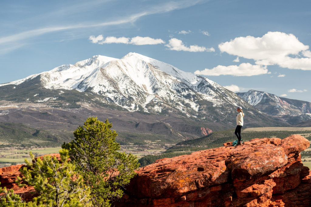 a woman stands on top of Red Hill in Carbondale Colorado with a view of Mount Sporis covered in snow in the background