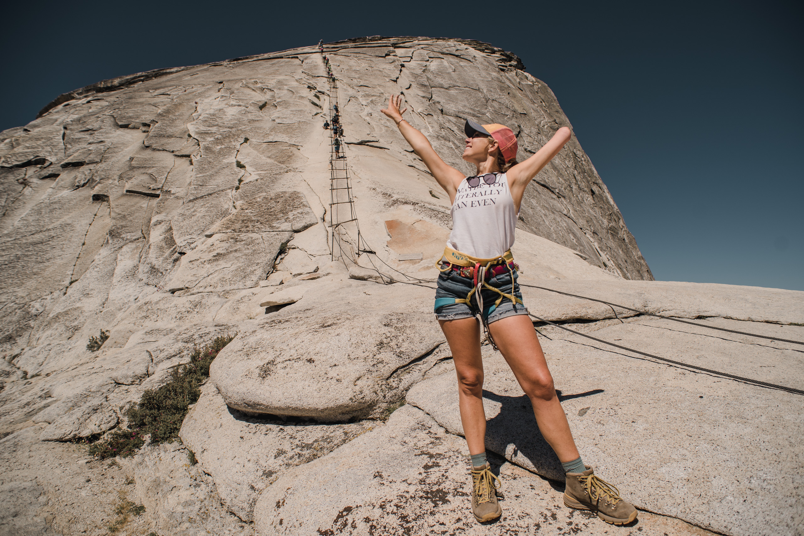 A woman stands at the base of the Half Dome Cables with her arms in the air