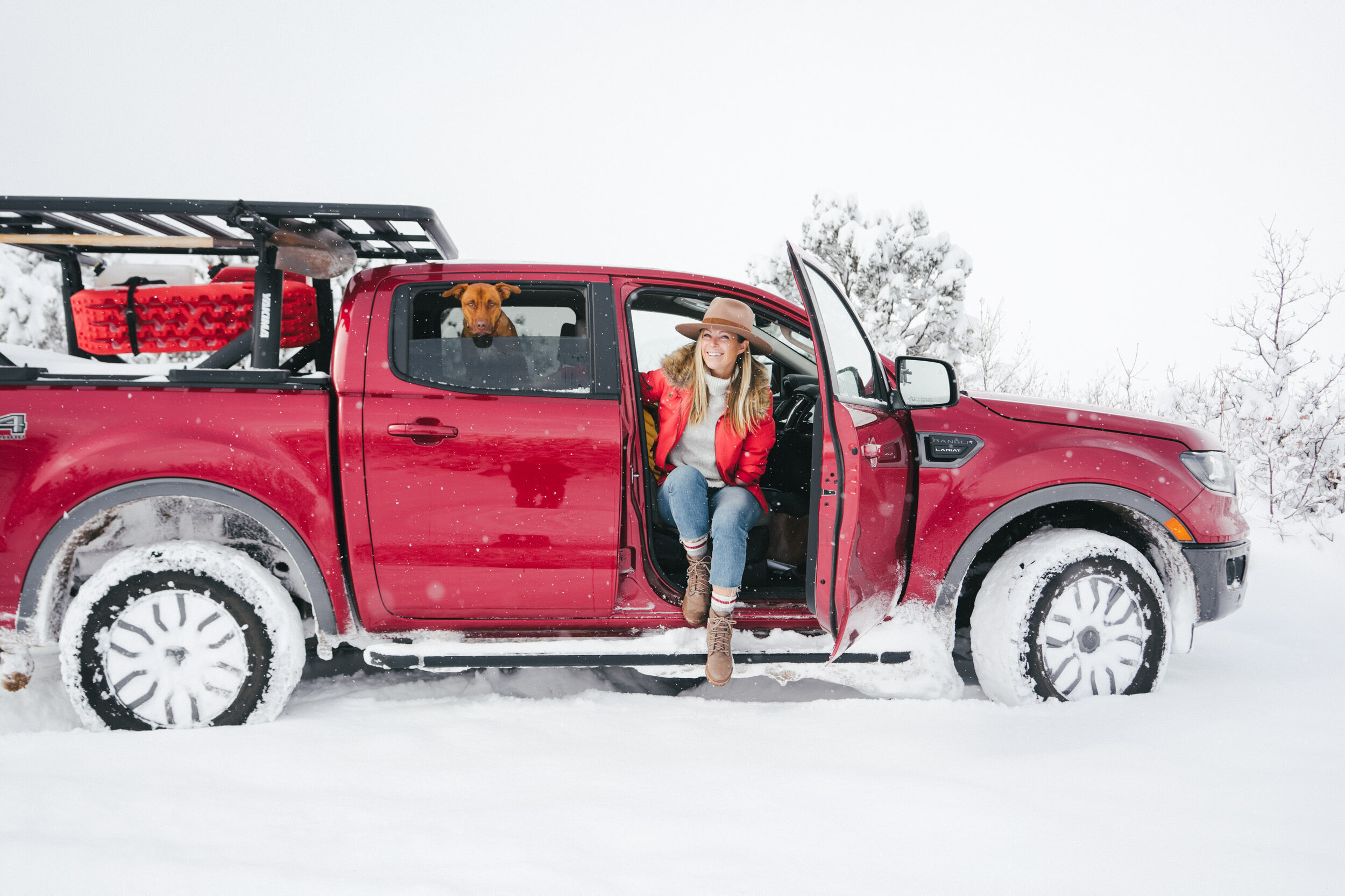 A woman sits in the passenger door of a red pickup truck in a blizzard snowstorm
