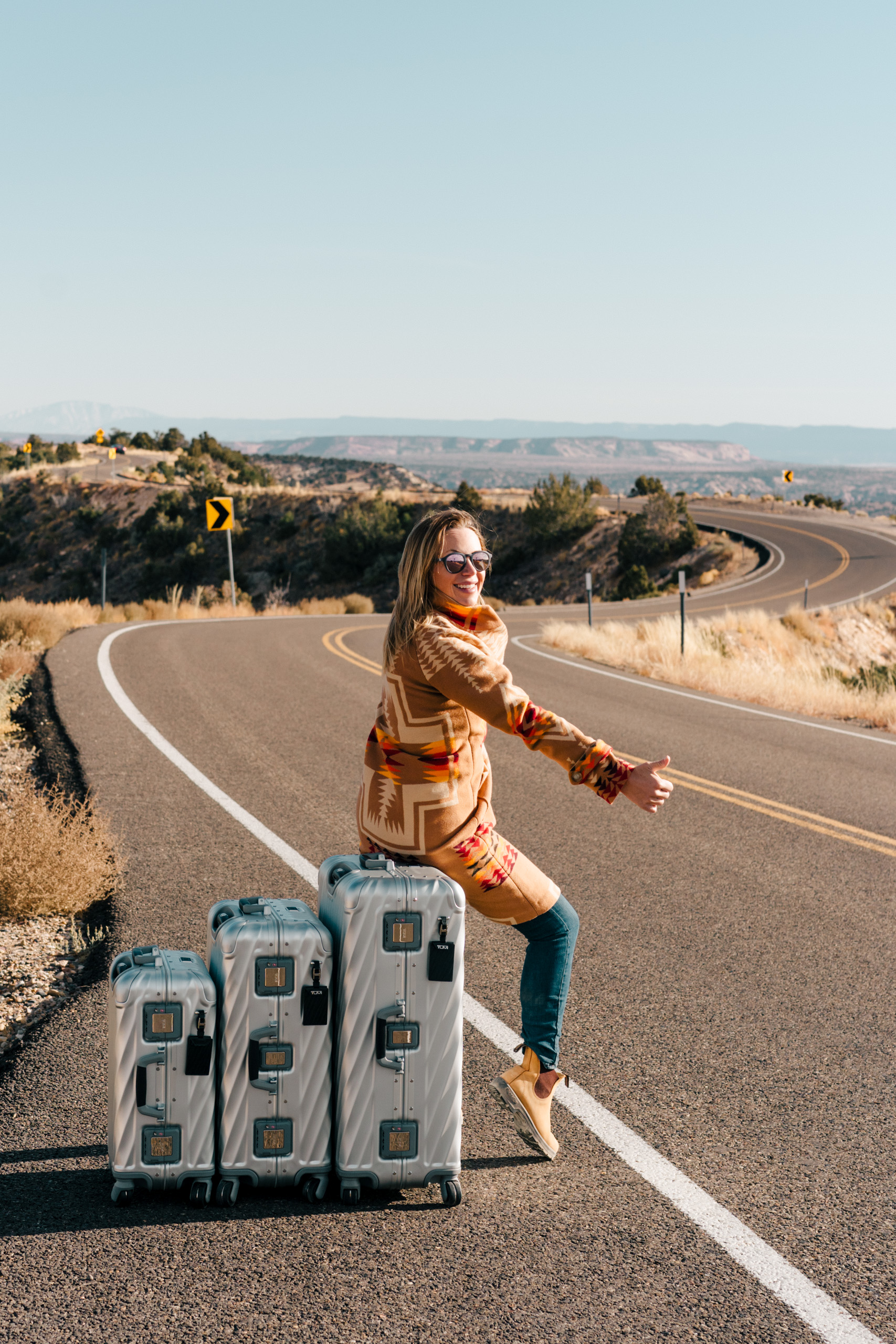 woman hitch hiking on the side of a windy road in the desert