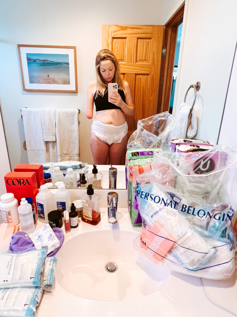 a woman wearing disposable diapers stands in the bathroom mirror after pregnancy loss
