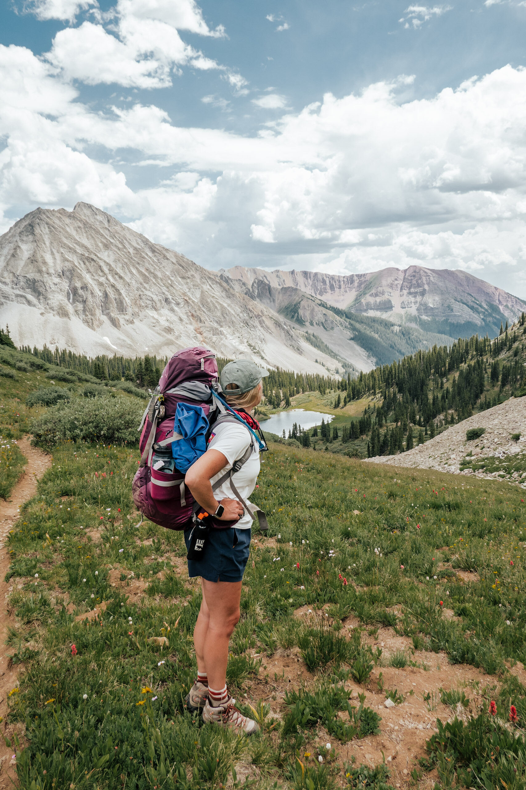 A woman wearing a backpack and hiking clothes takes in the view from the top of West Maroon Pass near Aspen Colorado