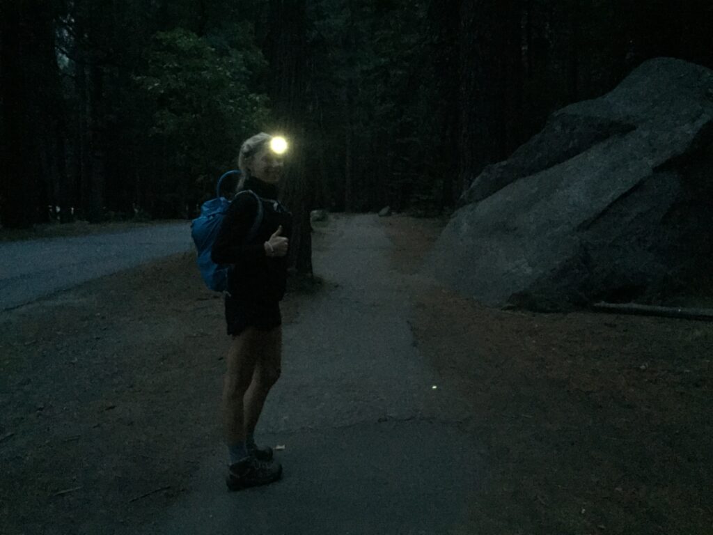 A woman wearing a headlamp and hiking clothes in the dark before sunrise to begin the hike up the half dome cables in yosemite national park