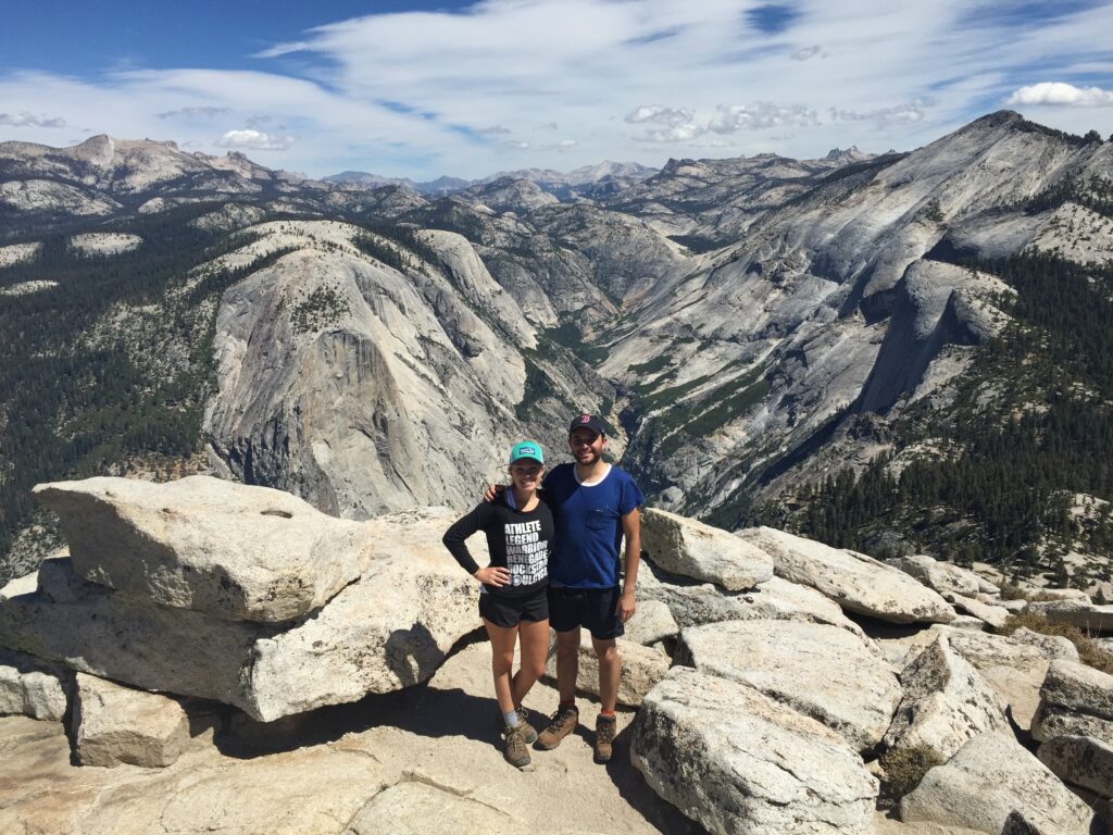 Friends stand on top of half dome with a view of the yosemite valley behind them